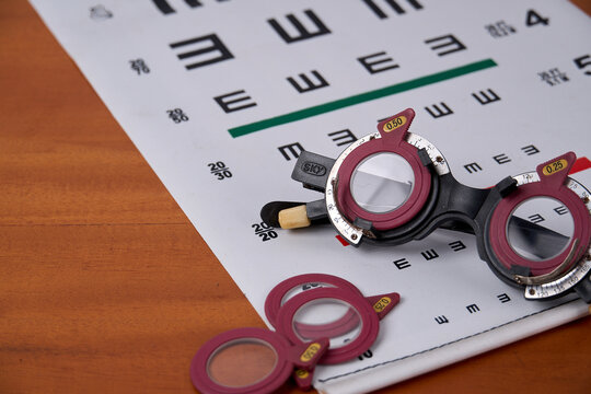 Optical trial frame with trial lenses on Snellen eye chart on wooden table