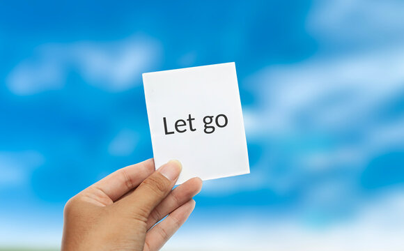Hand holding let go card message against bright blue sky background