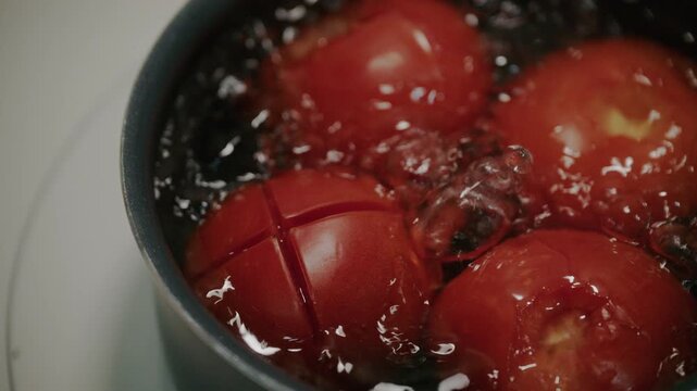 Close up shot of fresh red tomatoes blanching in boiling water in pot.