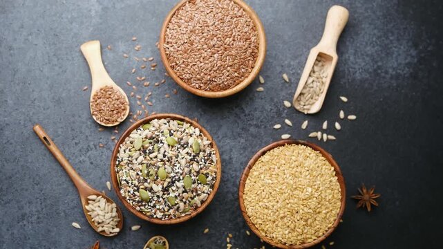 Assortment of seeds in wooden bowls and spoons arranged on a dark background