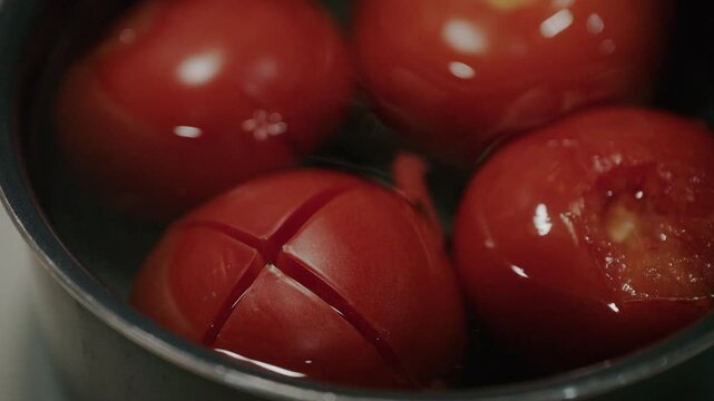 Close up shot of fresh red tomatoes blanching in boiling water in pot.