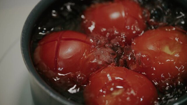 Close up shot of fresh red tomatoes blanching in boiling water in pot.
