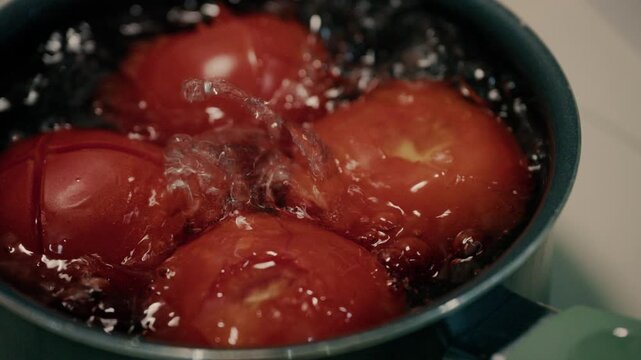 Close up shot of fresh red tomatoes blanching in boiling water in pot.