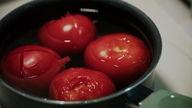 Close up shot of fresh red tomatoes blanching in boiling water in pot.
