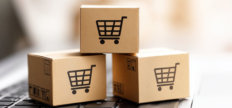 Three small shipping cardboard boxes with a shopping cart on them on the laptop as a symbol of fast delivery, online shopping and e-commerce