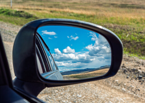 View of landscape reflected in side mirror while driving on gravel road