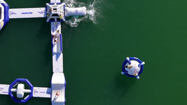 Cascais, Lisbon, Portugal - 02 July 2026: Aerial view of inflatable water park with people playing on floating obstacles in the sea.