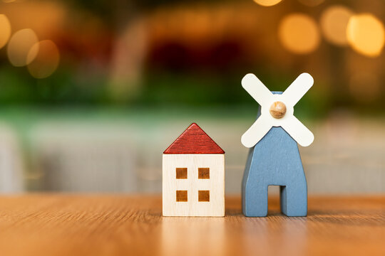 Eco friendly green home real estate concept with wooden house model and miniature windmill on wooden table with warm blurred background for clean energy housing
