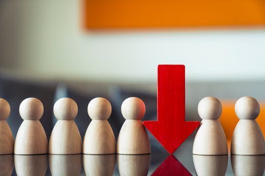 Human resource reduction and downsize concept with red arrow pointing down between wooden peg dolls on shiny table for staff lay off and business recession
