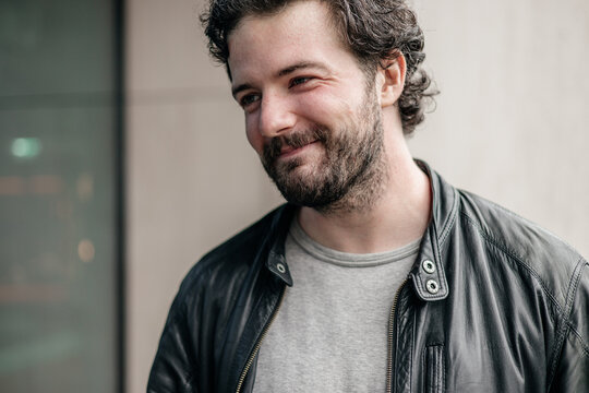 Close-up portrait of smiling bearded young man in casual clothing, authentic male expression, modern lifestyle and confidence outdoors
