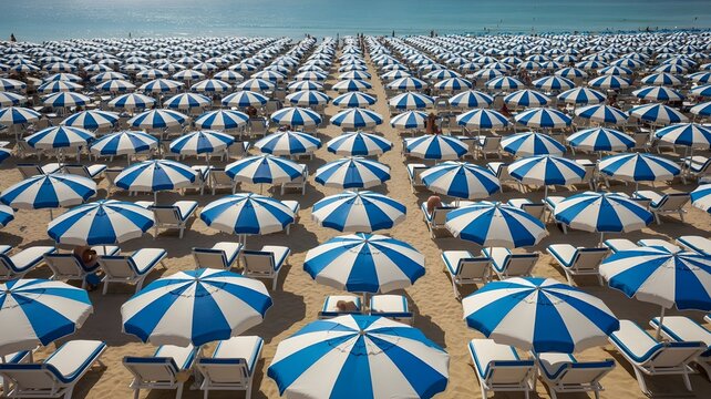 Crowded beach with rows of blue and white striped umbrellas during a sunny summer bank holiday weekend