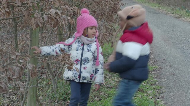 Two young children in winter clothing walking on a path through a forest