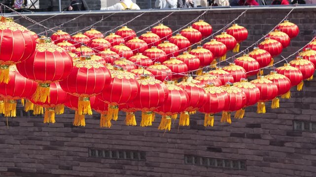 Rows of vibrant red Chinese lanterns hanging against an ancient brick wall background.