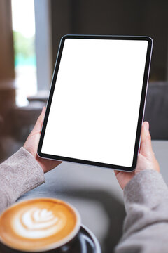 Vertical mockup image of a woman holding digital tablet with blank white desktop screen in cafe