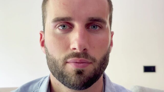 Captivating close-up portrait of a handsome bearded man with intense blue eyes, slowly opening them and looking directly at the camera with a confident and serene expression