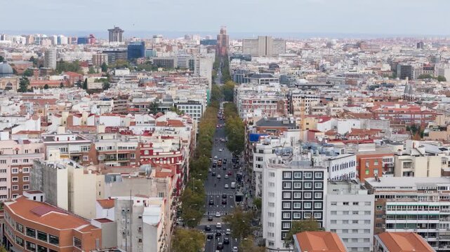 Madrid, Spain - 12 June 2026: Aerial view of a long tree-lined boulevard with traffic and dense residential buildings under a clear sky in the city center.
