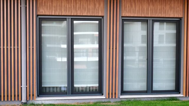 Modern exterior wall with wooden cladding and large glass windows featuring mosquito nets and blinds