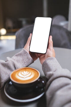 Vertical mockup image of a woman holding mobile phone with blank desktop screen in cafe