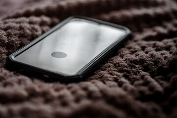Smartfon leżący na miękkim, dzianinowym kocu. Cyfrowy detoks, praca zdalna z domu, odpoczynek i nowoczesny styl życia w domowym zaciszu. © Henryk Niestrój