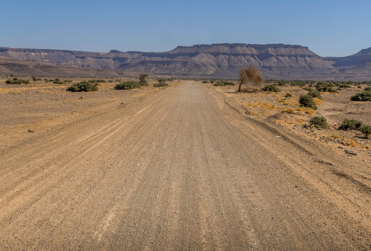 Desert road in Adrar Plateau, West Africa, in Mauritania landscape with sandstone rocks in the horizon, nearby Atar.
