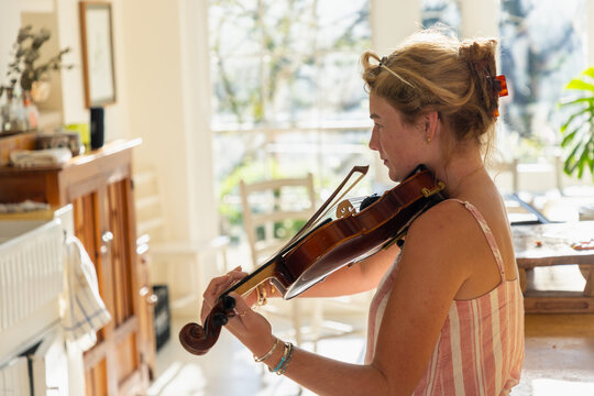young woman playing violin in light filled kitchen