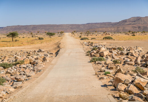 Desert road in Adrar Plateau, West Africa, in Mauritania landscape with sandstone rocks in the horizon, nearby Atar.
