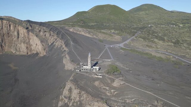Aerial view of lighthouse surrounded by volcanic landscape and rugged hills in daylight