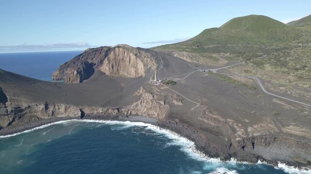 Aerial view of volcanic coastline with lighthouse, rugged cliffs, and ocean waves