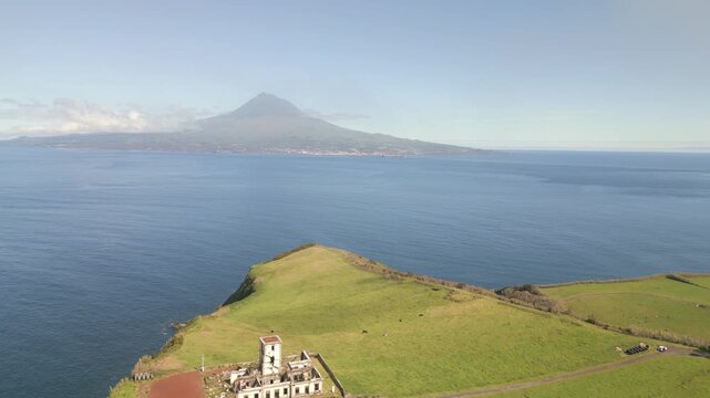 Aerial Reveal, Lighthouse of Ribeirinha on Faial Island, Azores, Portugal, overlooking the Atlantic Ocean with Pico Mountain visible across the water