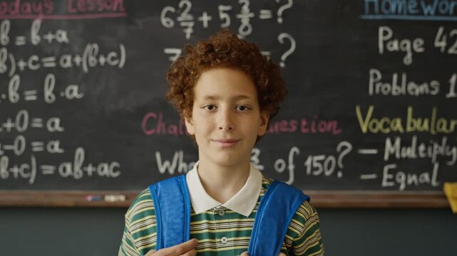 Portrait of Caucasian boy standing in front of African Americanboard with math formulas, adjusting backpack straps and smiling. Footage is perfect for elementary school ads or educational marketing