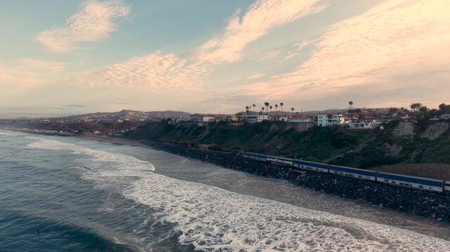 A dramatic cinematic drone shot captures the Pacific Surfliner train traveling along the breathtaking Southern California coastline from San Clemente to San Juan Capistrano.