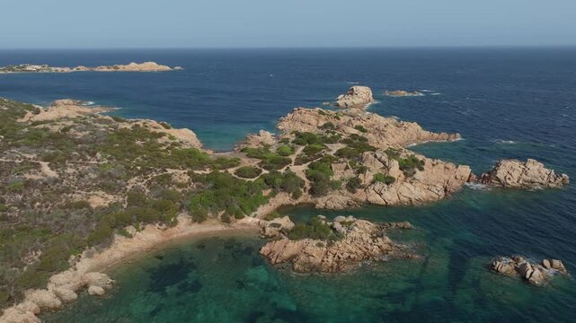 Stunning aerial shot slowly panning over the rugged pink granite coastline of Sardinia, revealing hidden coves with crystal clear water