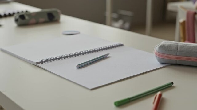 School supplies including open notebook, pen, and pencil case resting on desk in modern classroom. Footage is suitable for back to school promotions and educational campaigns