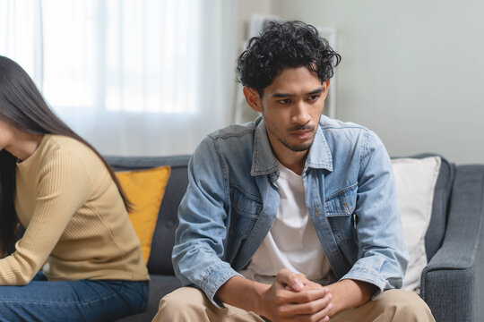 Family problem concept. Tension in relationship between married couple, husband and wife staying sitting separate after quarrel in the living room.