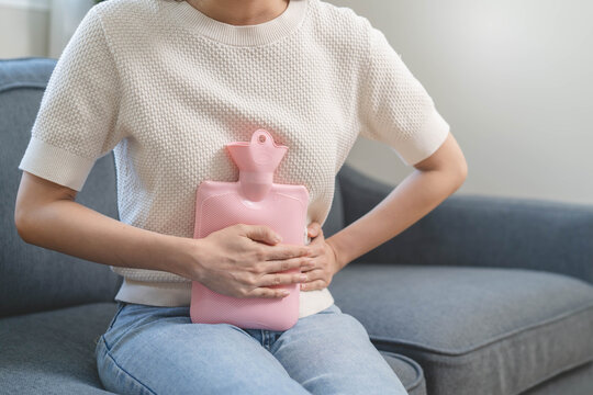 Close-up hands of young woman putting on her belly and feeling pain from cycle period on the sofa.