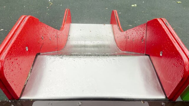 rain hits the metallic surface of the slide, making a soft tapping sound. The deserted and wet play area brings a peaceful, nostalgic, and lonely feeling.