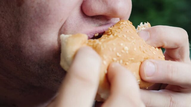 Close up of person taking a big bite out of a sesame seed hamburger with their hands.