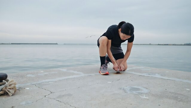 Young Man Bending Over and Picking Up Object on Seaside Shore Under Overcast Sky