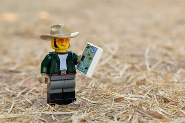 Fototapeta premium Lego minifigure of happy boy tourist with map is walking in the natural dried grass field. Editorial illustrative image of popular plastic toy.