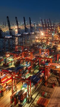 Asia, China, Hong Kong, cityscape vertical time lapse of busy shipping cargo container port, with cranes unloading and loading cargo at night