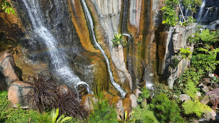 a majestic waterfall cascades down steep, moss-covered cliffs with bright sunlight shining through and lush green vegetation © umi