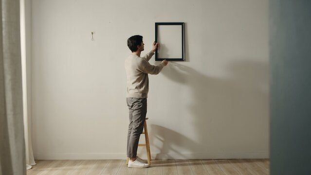 Woman Hanging Empty Picture Frame on Minimalist Wall Interior