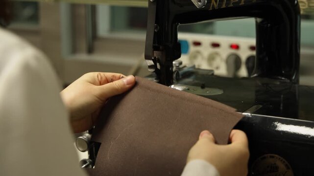 A close-up of a craftsperson's hands working on a leather piece near a sewing or crafting machine in a leather workshop.