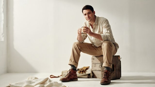 Young Man Sitting on Wooden Box Drinking Coffee in Studio Setting