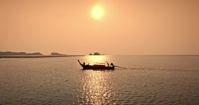 Longtail boat silhouette sailing against golden hour sunset sky, calm Andaman Sea water with distant islands capture serene travel and tourism moments in Thailand. Travel and explore Koh Lanta Island