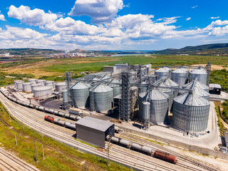 Grain storage facility with many silos located by train tracks in a rural area under a bright sky © DSMT
