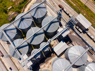Storage silos are seen from above with trains in the background during the day in an industrial area © DSMT