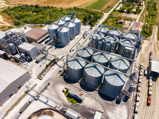 View of grain storage facility with silos and warehouse near farmland on a sunny day © DSMT
