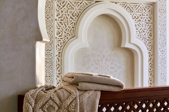 Hand-woven cotton towels draped over a dark teak rail, showcasing a Moroccan riad bathroom with intricate plaster arch detail