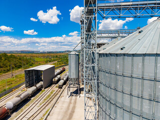 Train cars parked near large metal silos at a storage facility on a sunny day in a rural area © DSMT